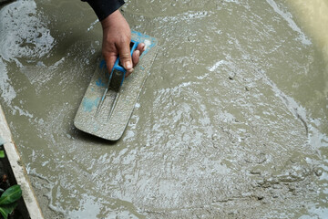 Hand worker holding trowel for smoothing plaster concrete floor.