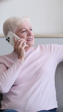 Senior Caucasian woman using cellphone for talking during call at home. Remote communication during spending happy leisure time. Vertical video.