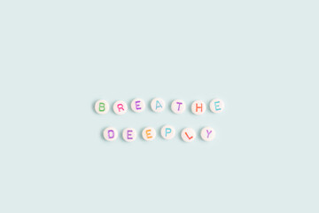 Breathe deeply. Quote made of white round beads with multicolored letters on a blue background.