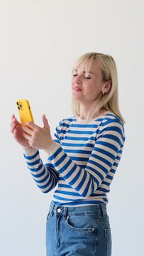 Happy Caucasian woman messaging in online social media or reading news, through the mobile phone and laughing on white background Vertical video.