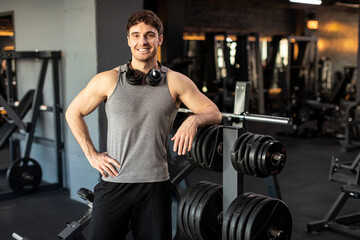 Handsome muscular man posing in gym, standing in modern sport club interior and smiling at camera,...