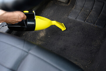 Close-up of man hand cleaning interior of a car using a portable vacuum cleaner. Man vacuums floor...