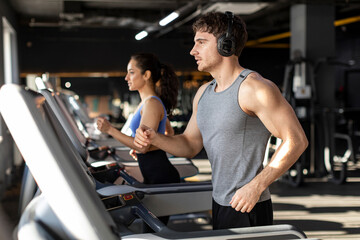 Music and exercises go together. Fit man and woman exercising on treadmill, enjoying morning workout