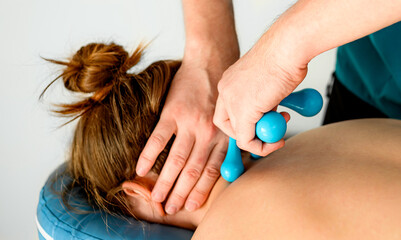 Masseur hands with massager tool doing neck massage to girl client. Body care treatment therapy procedure for wellness and relaxation in spa salon clinic.