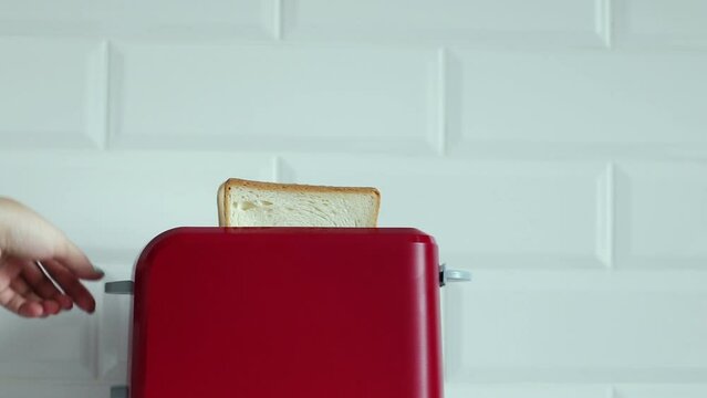 Woman hand putting two pieces in red bright toaster, Roasted toast bread popping up from toaster machine with smoke. Prepare breakfast. Two toast pieces popping out from toaster