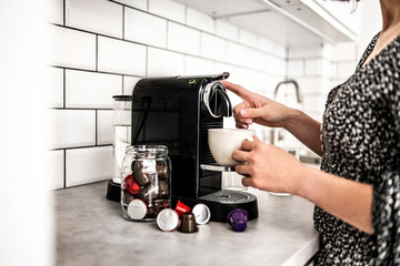 Girl with capsule coffee machine and cup at kitchen. Woman preparing italian caffeine beverage using professional espresso maker