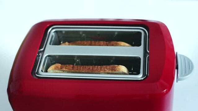 Roasted toast bread popping up from bright red toaster machine. Two toast pieces popping out from toaster 