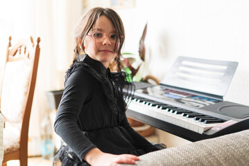Portrait of a cute little girl sitting at home and playing the piano