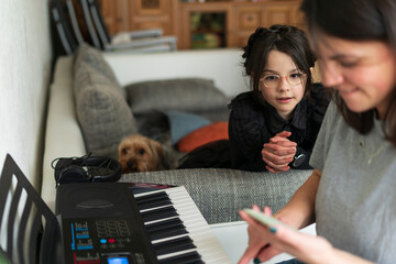 Mother and daughter playing piano at home. Focus on the girl.