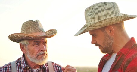 Portrait view of the two farmer engineers wearing hat examining plants and controlling water system in the field while standing and discussing. Organic farm business concept