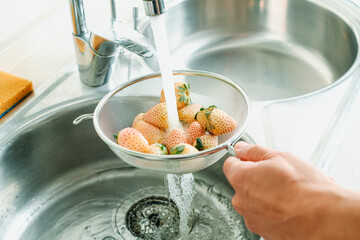 man rinses some white strawberries in a colander - 796604292