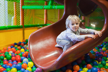 Toddler having fun in a green ball pit at the playground. Cute Kid Or Child Playing Colorful Balls...