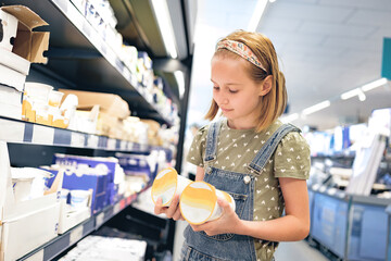 Pretty girl child choosing yogurt in supermarket shop. Beautiful female preteen kid looking milk products in grocery store