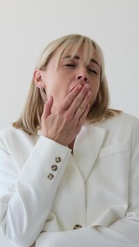 Tired Caucasian woman yawning and stretching on white background. Boredom, burnout, tiredness and sleepless concept. Vertical video.