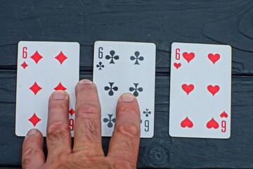 three playing paper cards six of hearts diamond and cross lie on a black wooden table with hand fingers