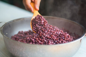 Woman's hand release temperature by using wooden ladle scoop boiled azuki beans in stainless steel...