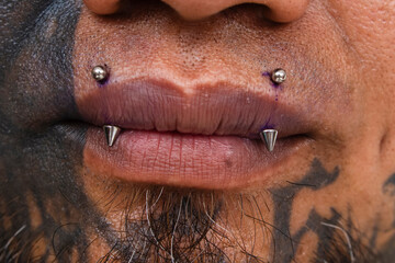 Example of angel fangs piercing on the upper lip of a heavily tattooed man.