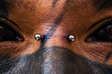 Closeup of a man covered with face tattoos, with a nose bridge piercing between his black eye...