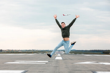 Concept of joyful and carefree travel. Happy man with arms up jumping on airport runway..
