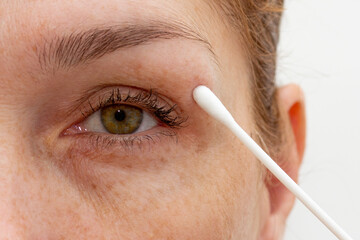 Close up cropped eye of middle aged caucasian woman looking at camera and holding cotton swab on...