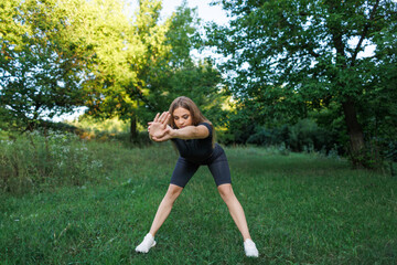 A young girl doing exercises in the park. Athletic girl in a tight uniform working outdoors in the park.
