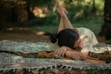 Photo of a girl lying on a mat in the forest and resting.