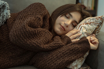 A girl in a brown winter dress is sleeping on a cozy couch.