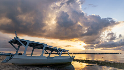 A boat rests on the sandy beach as the sunset over the horizon
