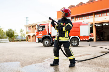 An adult Caucasian woman works as a firefighter at a fire station dressed in a uniform.The senior woman is practicing with the pressurized water hose inside the fire station.