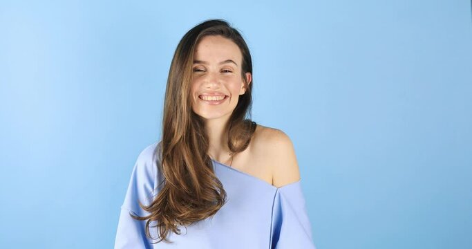 Okay! Playful attractive brunette woman showing ok and smiling, winking to camera, gesturing all right, agree sign, approving right choice isolated on blue background. All right!