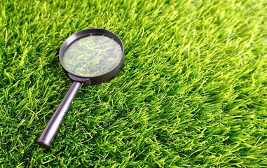 Magnifying glass with black frame and handle on top of grass field horizontal ratio background....