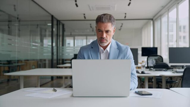 Busy middle aged professional business man ceo, 50 years old businessman executive wearing blue suit using laptop computer thinking on financial investment working in corporate office. Authentic video
