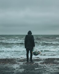 On the beach, an anonymous silhouette holds a plastic bag of discarded items, representing a message of hope and action for our oceans