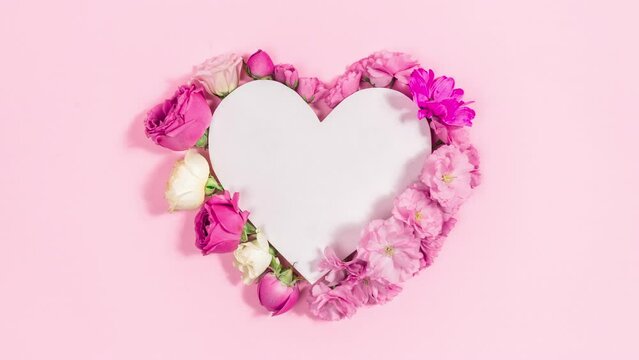 Natural roses and sakura flowers appear near white paper heart. Greeting card for mother's, women's, birthday day or other occasion. Stop motion animation. Copy space. Flat Lay.
