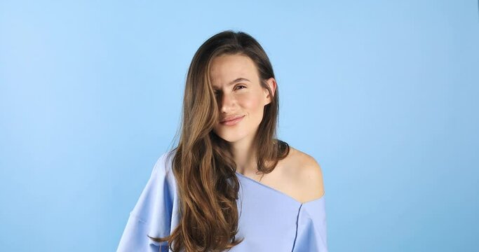 Attractive brunette woman isolated on blue background. Curious, suspicious, woman look at camera, knocking. Confused smiling female.