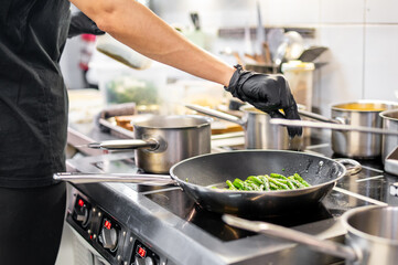 Professional chef sautéing fresh green vegetables in a dynamic kitchen environment, showcasing...
