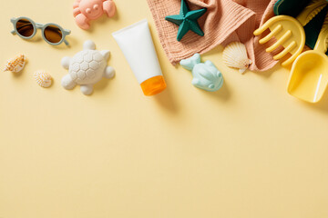 Flat lay composition with tube of sunscreen cream, sand beach toys, sunglasses on pastel beige background. Sun protection for kids concept.
