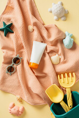 Tube of sunscreen cream, children's sunglasses and beach toys on beige table. Kids sun protection concept. Flat lay, top view.