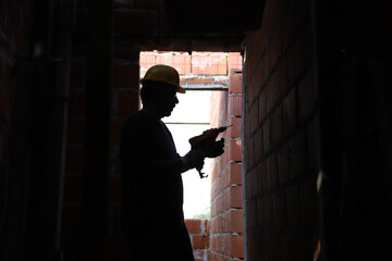 Backlight of worker drilling a wall with an electric drill. Builder working on construction site....