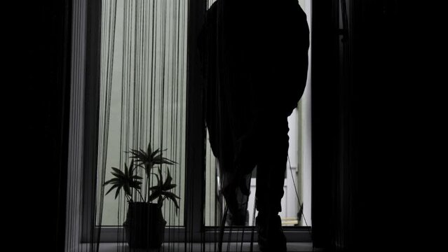 A thief or bandit in a mask breaks open a window with a crowbar and breaks into the house.