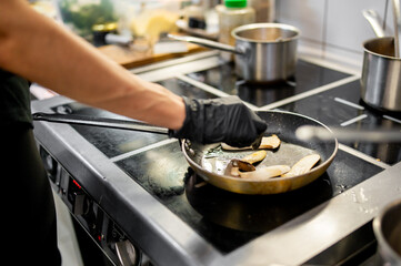 Professional chef skillfully sautéing sliced mushrooms in a pan on a stove, capturing the essence of culinary art.