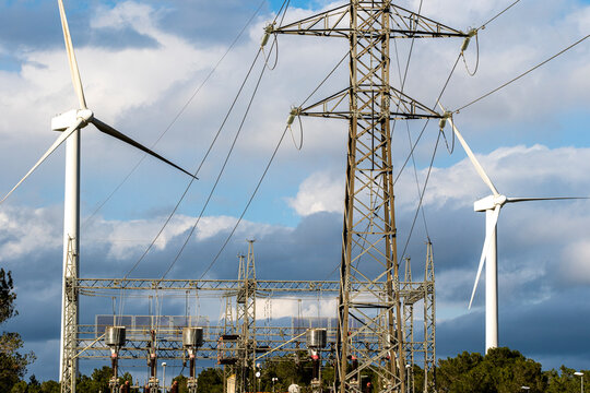 This image from Tarragona, Catalonia, Spain, showcases the powerful blend of traditional electricity infrastructure alongside modern green energy wind turbines demonstrating environmental consciousne