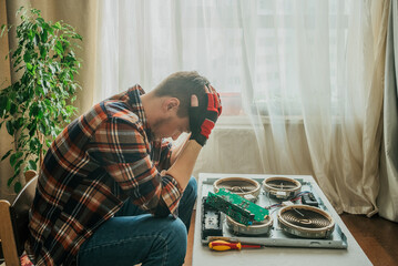 Man appears pensive as he pauses during the intricate process of repairing stove cooktop, scene of indoor troubleshooting. Master cannot find the cause of the breakdown and does not know where to
