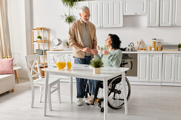 A disabled woman in a wheelchair talking with her husband in the warm ambiance of their kitchen at...