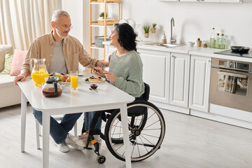 A man in a wheelchair and a woman sitting together at a table in their kitchen at home.