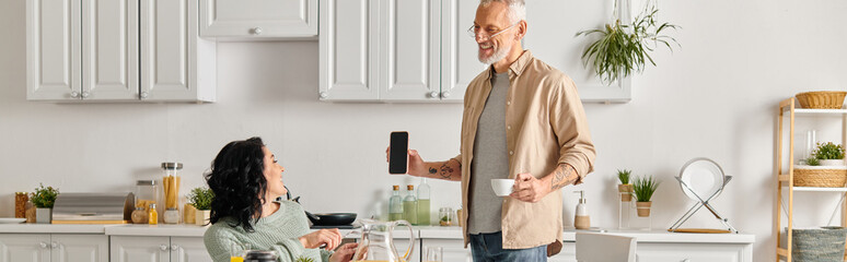 A man and a woman, the latter in a wheelchair, stand together in a cozy kitchen at home.