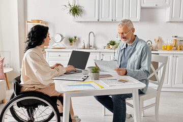 A woman in a wheelchair converses with a man in a cozy kitchen at home, sharing a moment of connection. - obrazy, fototapety, plakaty