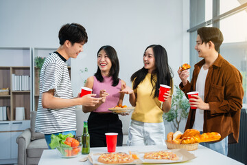 .Young Asian students gather with friends for a pizza party, laughing and sharing slices. Enjoying...