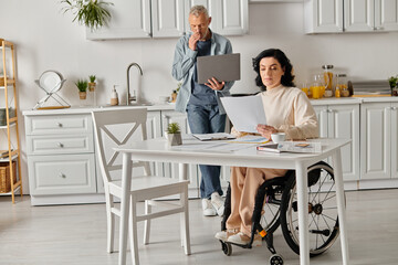 A disabled woman in a wheelchair interacts with a laptop, supported by her husband in a cozy...
