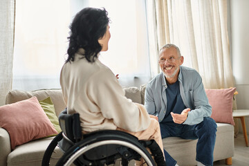 A woman in a wheelchair engages in conversation with her husband in their cozy living room setting.